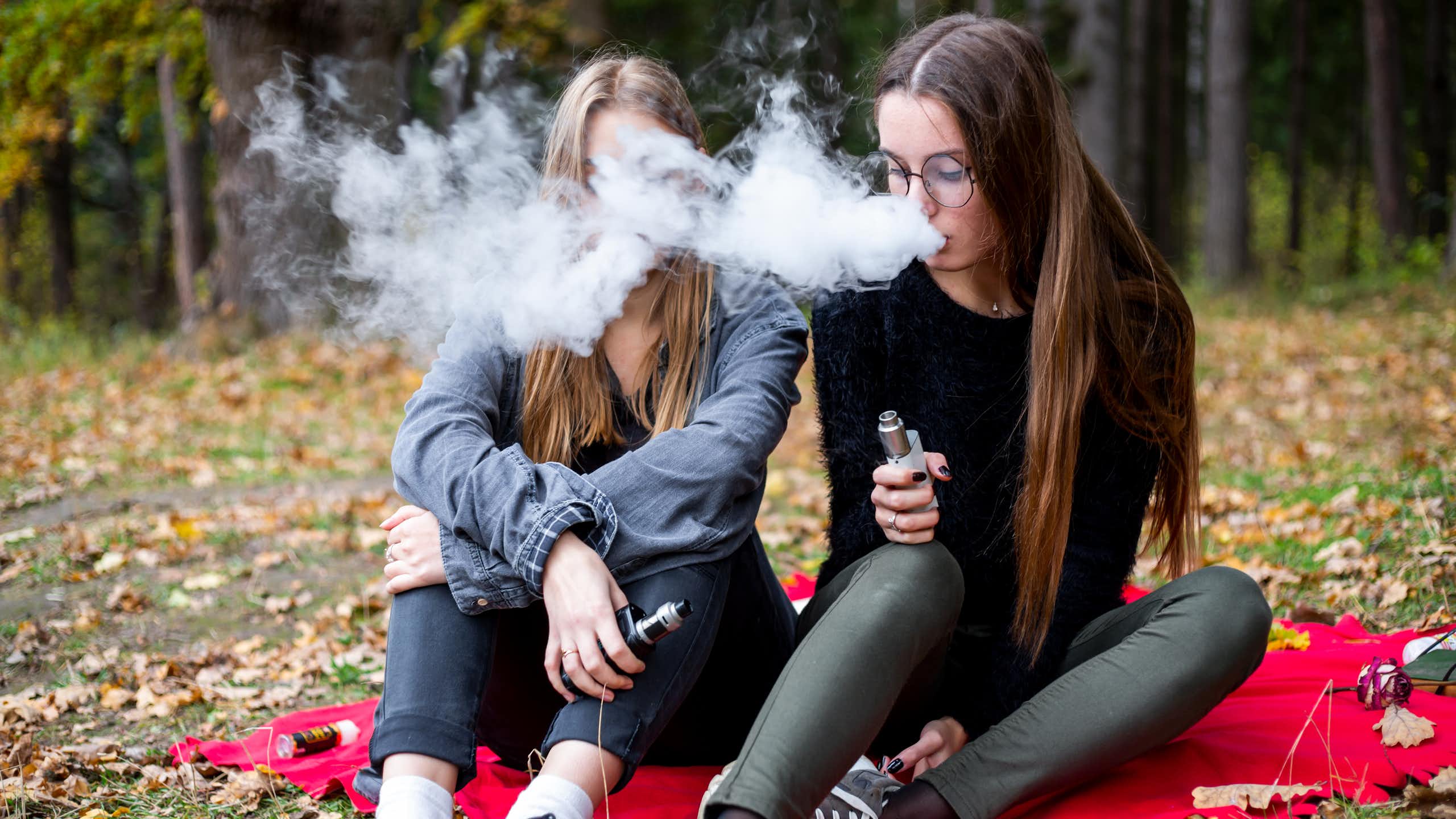 Two teenage girls vaping in park
