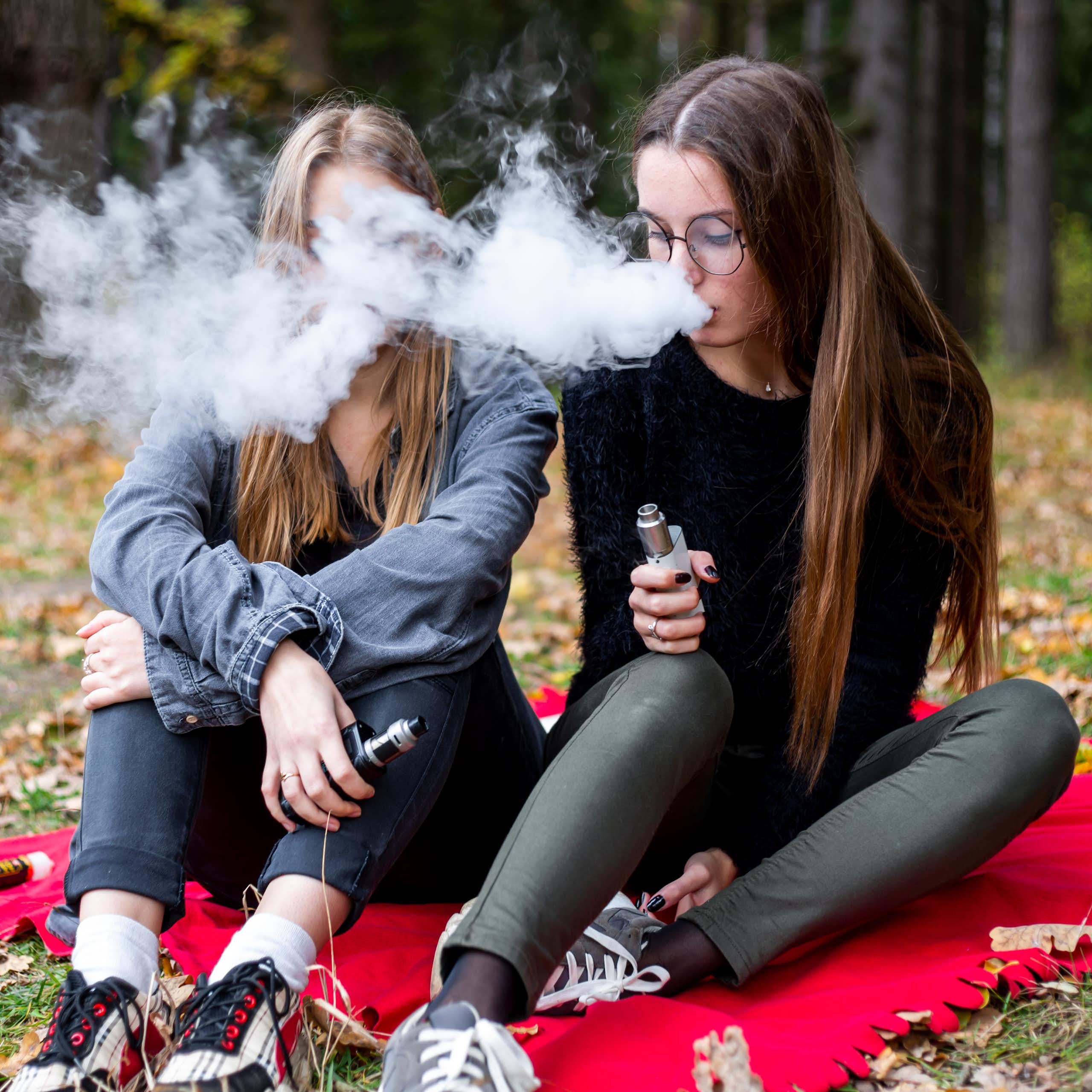 Two teenage girls vaping in park