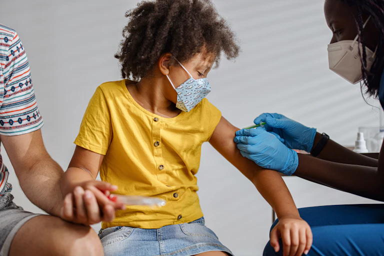 Masked child getting vaccinated by a masked clinician