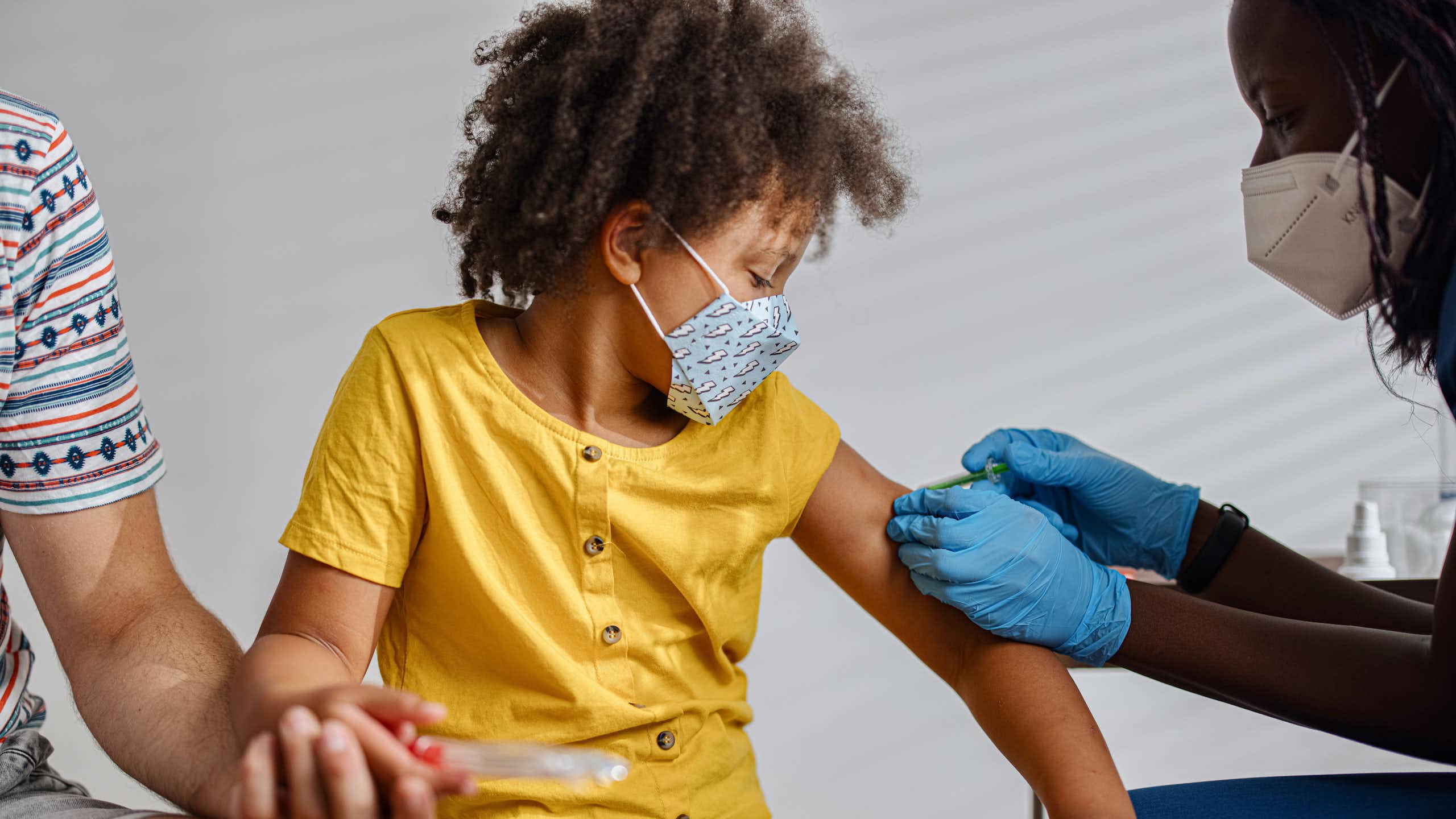 Masked child getting vaccinated by a masked clinician
