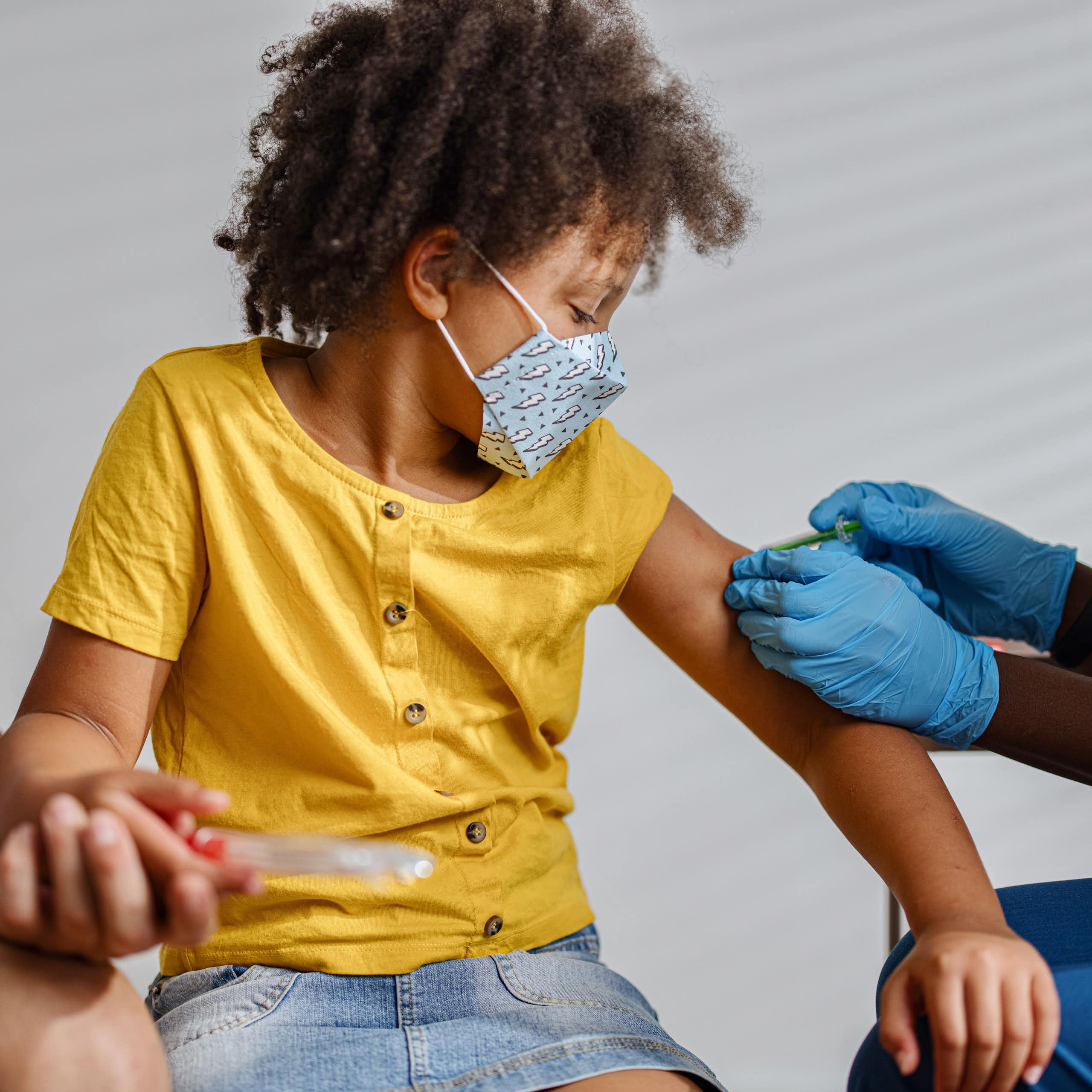 Masked child getting vaccinated by a masked clinician