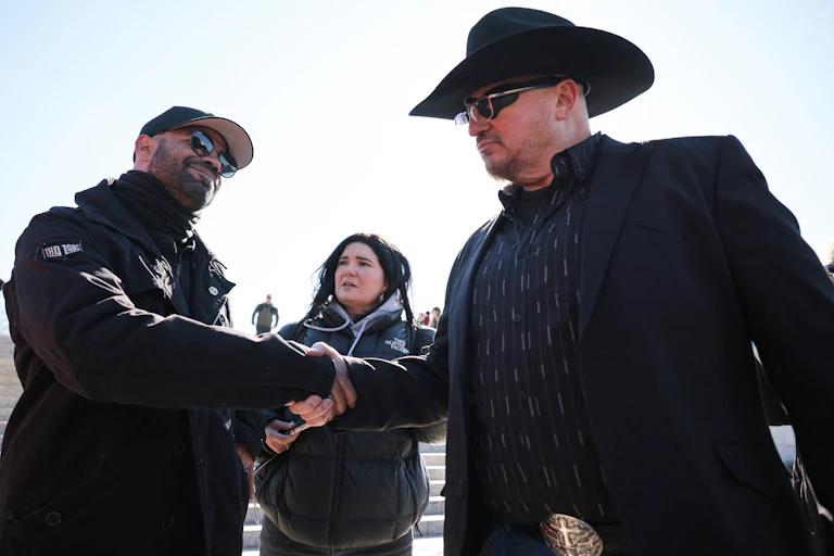 Two men dressed in black shake hands.
