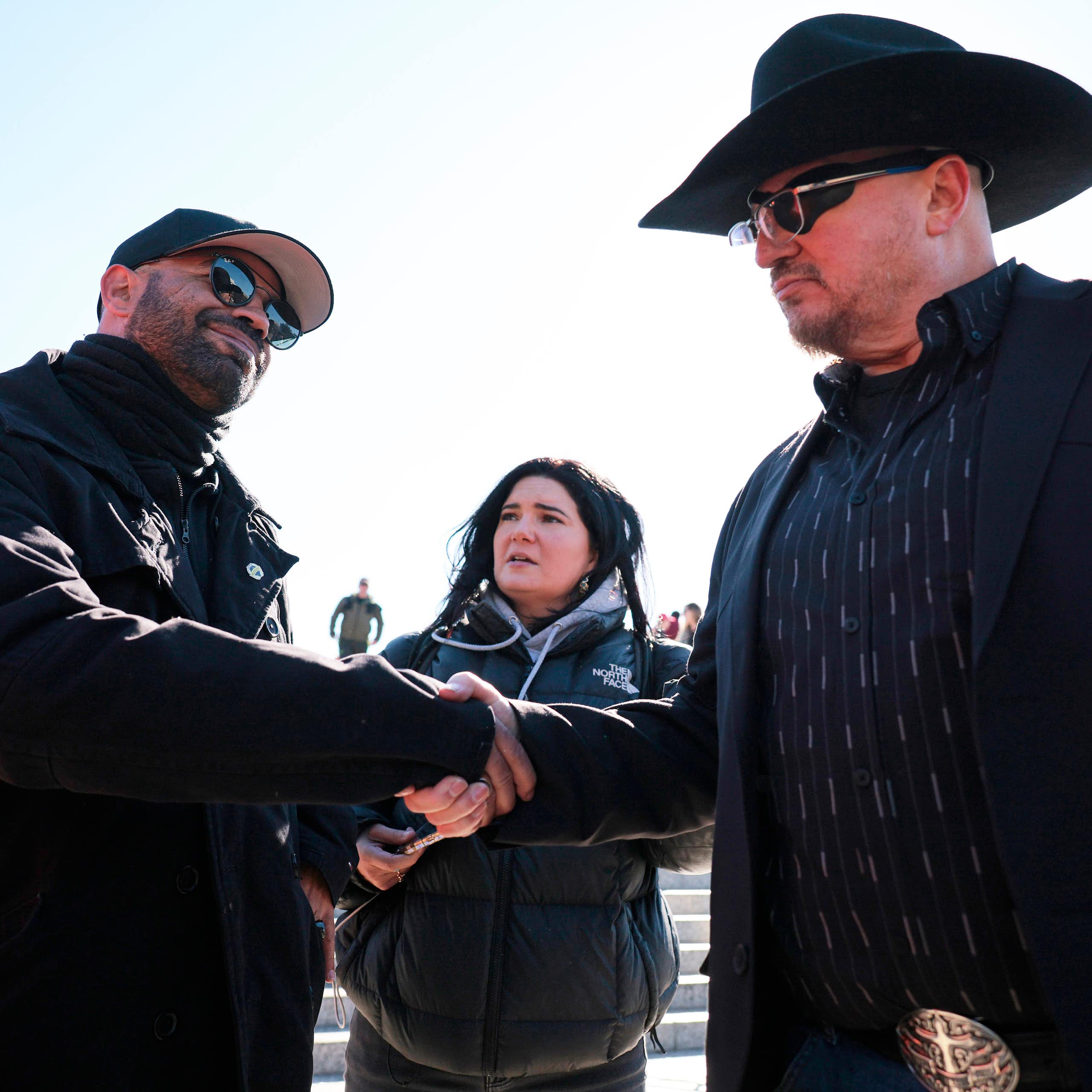 Two men dressed in black shake hands.