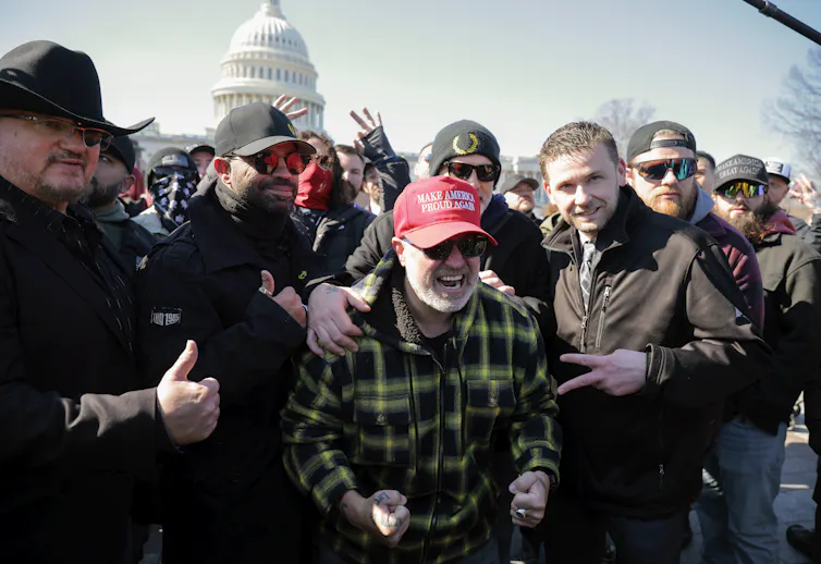 Several men wearing hats cheer in front of a federal building.