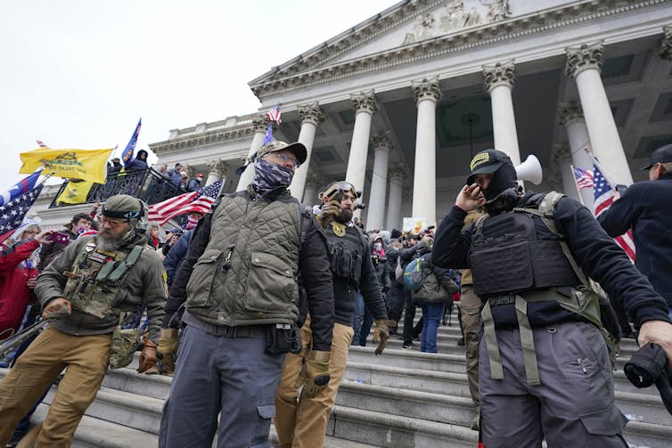 Several men dressed in military gear stand in front of a federal building.