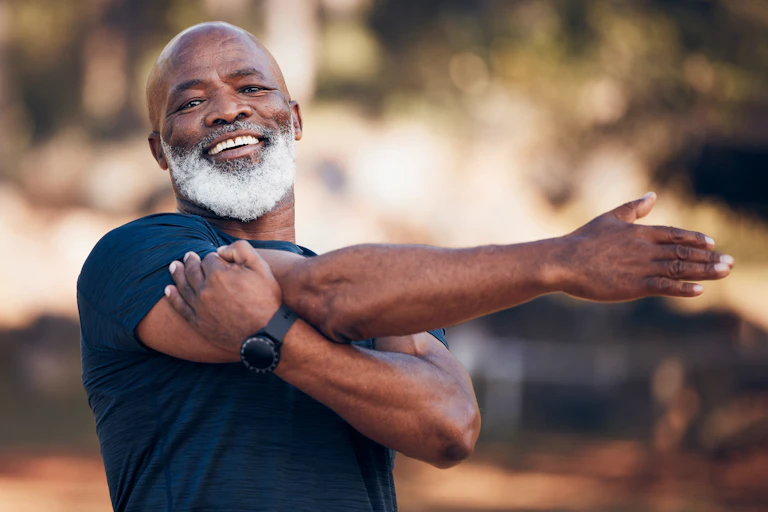 Smiling man with white beard does stretching exercises outdoors