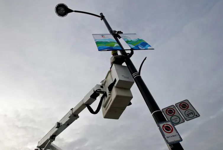 An electrician in a cherry-picker hangs banners on a light standard.