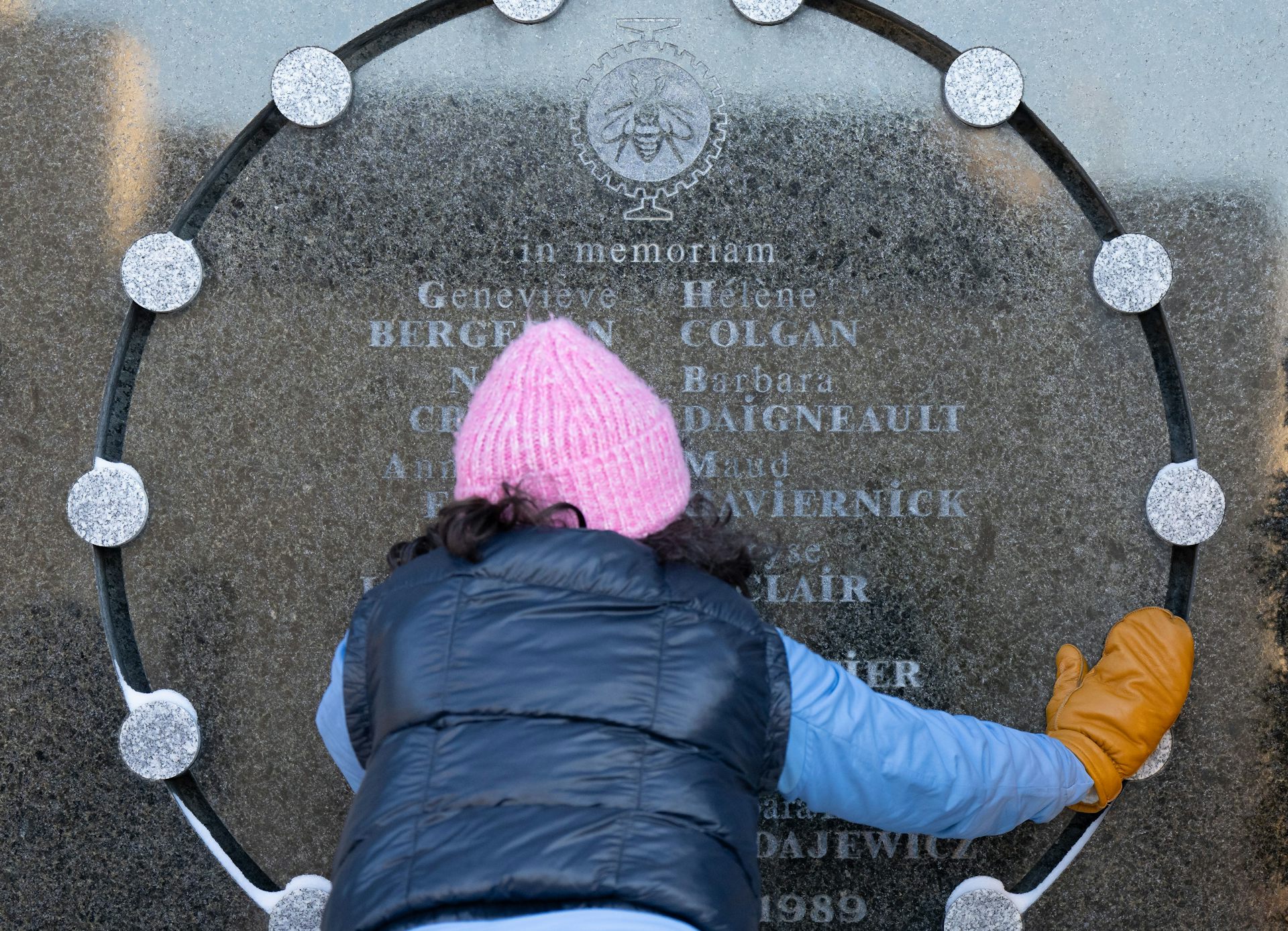 Una mujer con un gorro de lana rosa aparece fotografiada detrás tocando los nombres grabados en el monumento de piedra.