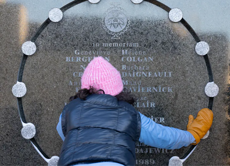 Una mujer con un gorro de lana rosa aparece fotografiada detrás tocando los nombres grabados en el monumento de piedra.