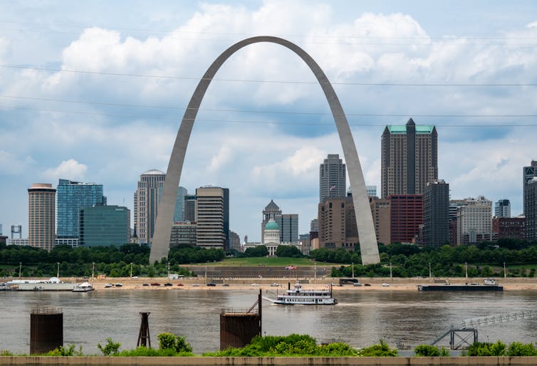 A large metal arch towers above a river with buildings in the background.