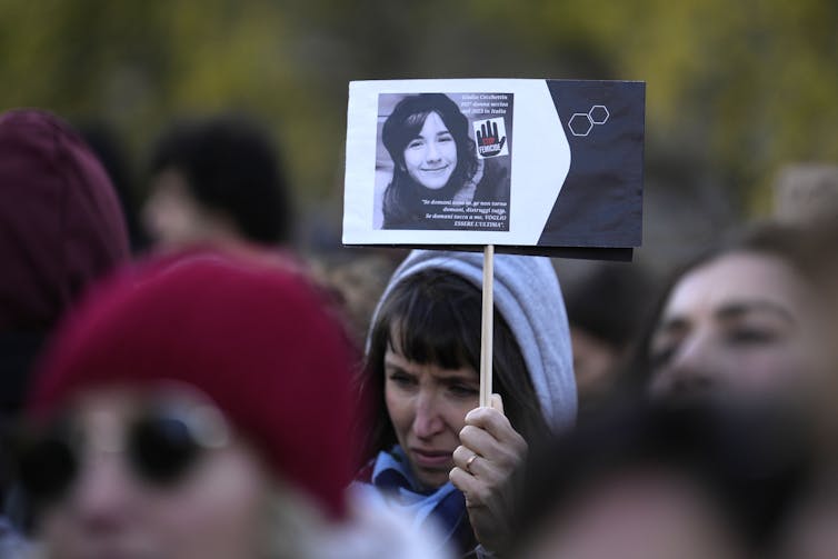 A weeping woman holds up a photo of a younger woman at a public gathering.
