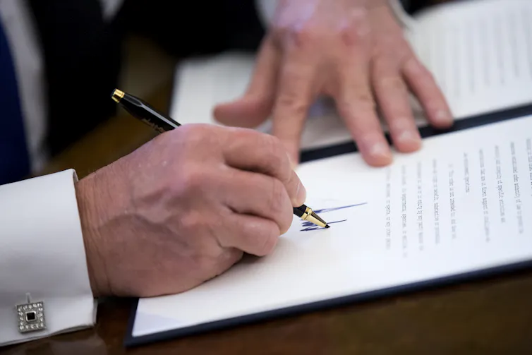 A close-up of a person holding a pen and signing a piece of white paper.