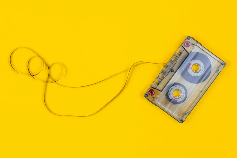 A cassette tape in front of a bright yellow background, with some of its tape unravelled.