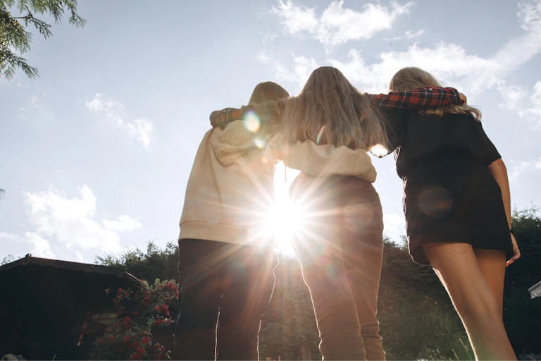 Teenagers outdoors with their arms around one another, with the Sun shining in the background