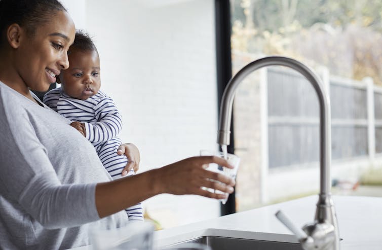PFAS in pregnant ladies’s ingesting water places their young children at upper chance, learn about reveals 1 A woman holding a small child fills a glass with water.