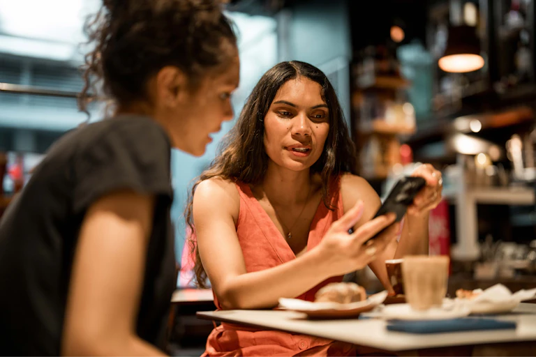 Two Indigenous women talking to a phone