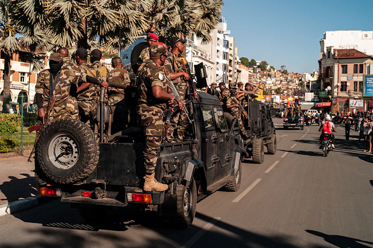 Armed men standing on the back of a truck that is part of a convoy driving through a street