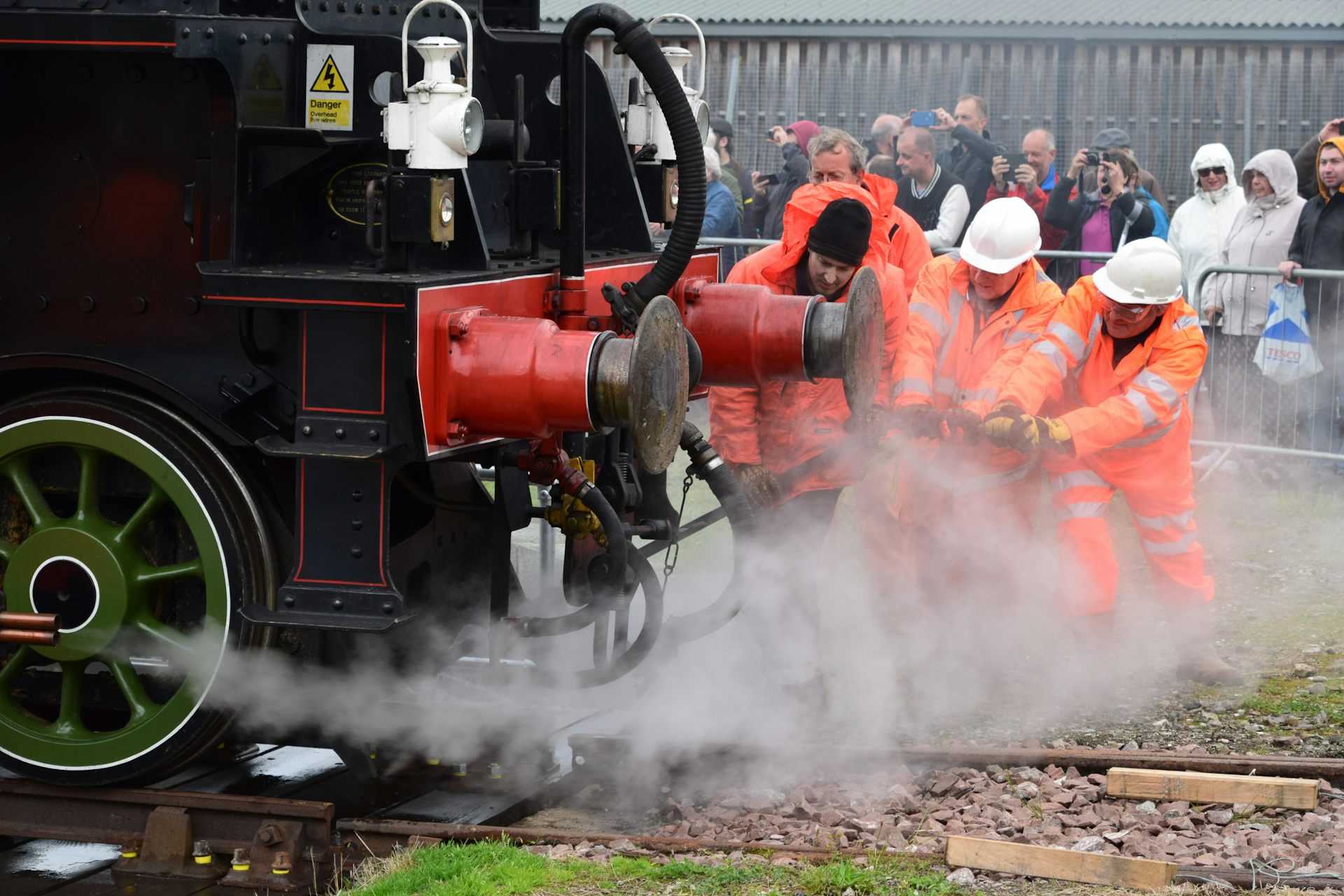 A group of men in hi-vis jackets pulling at a component of a steam engine