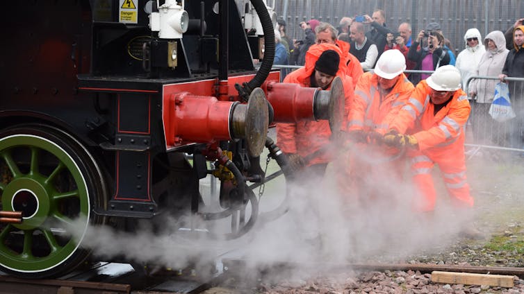 A group of men in hi-vis jackets pulling at a component of a steam engine