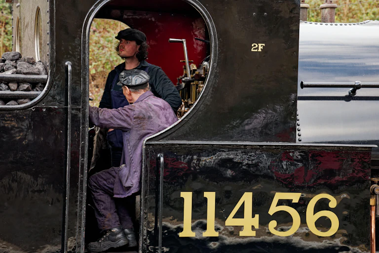 A young and older man in the driver's carriage of a steam engine