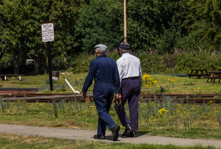 View from behind of two older men walking side by side towards the railway track