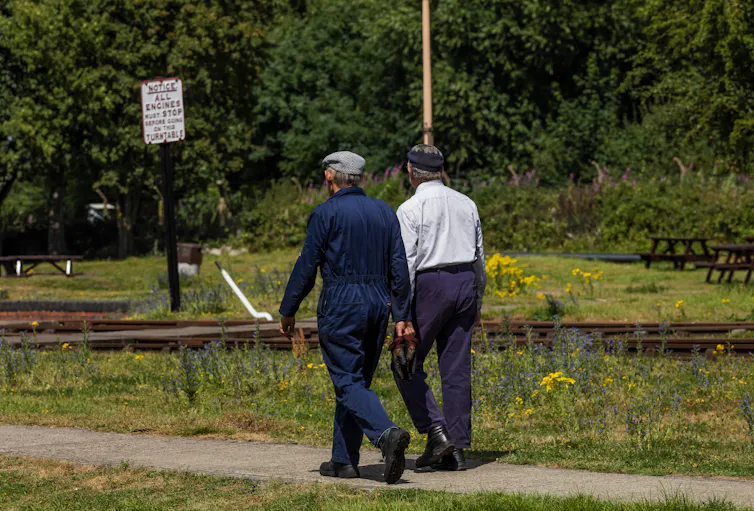 View from behind of two older men walking side by side towards the railway track