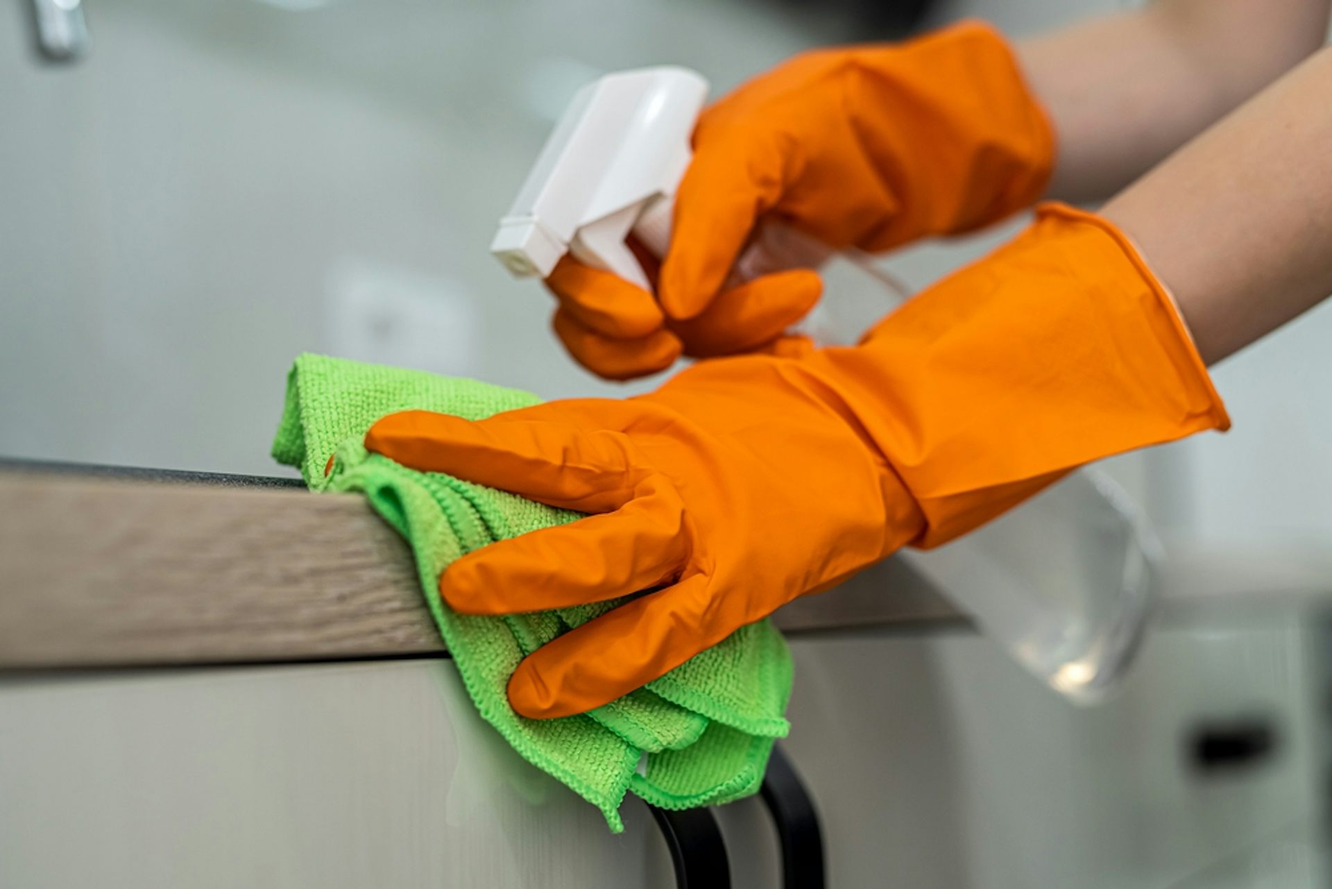 Person wearing rubber gloves, spraying a kitchen-counter top with antibacterial spray.