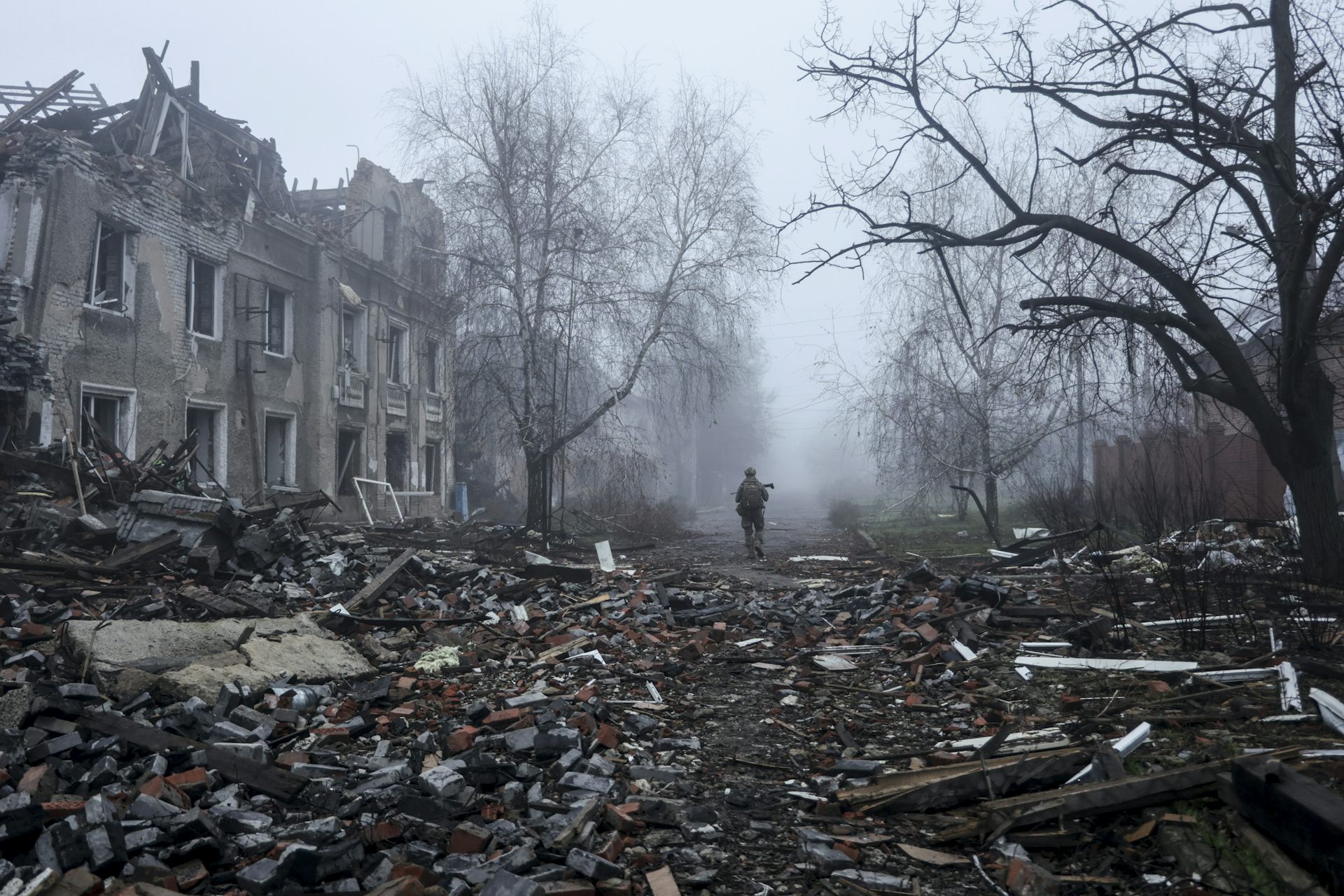 A Ukrainian soldier walks down a damaged street on a foggy day.