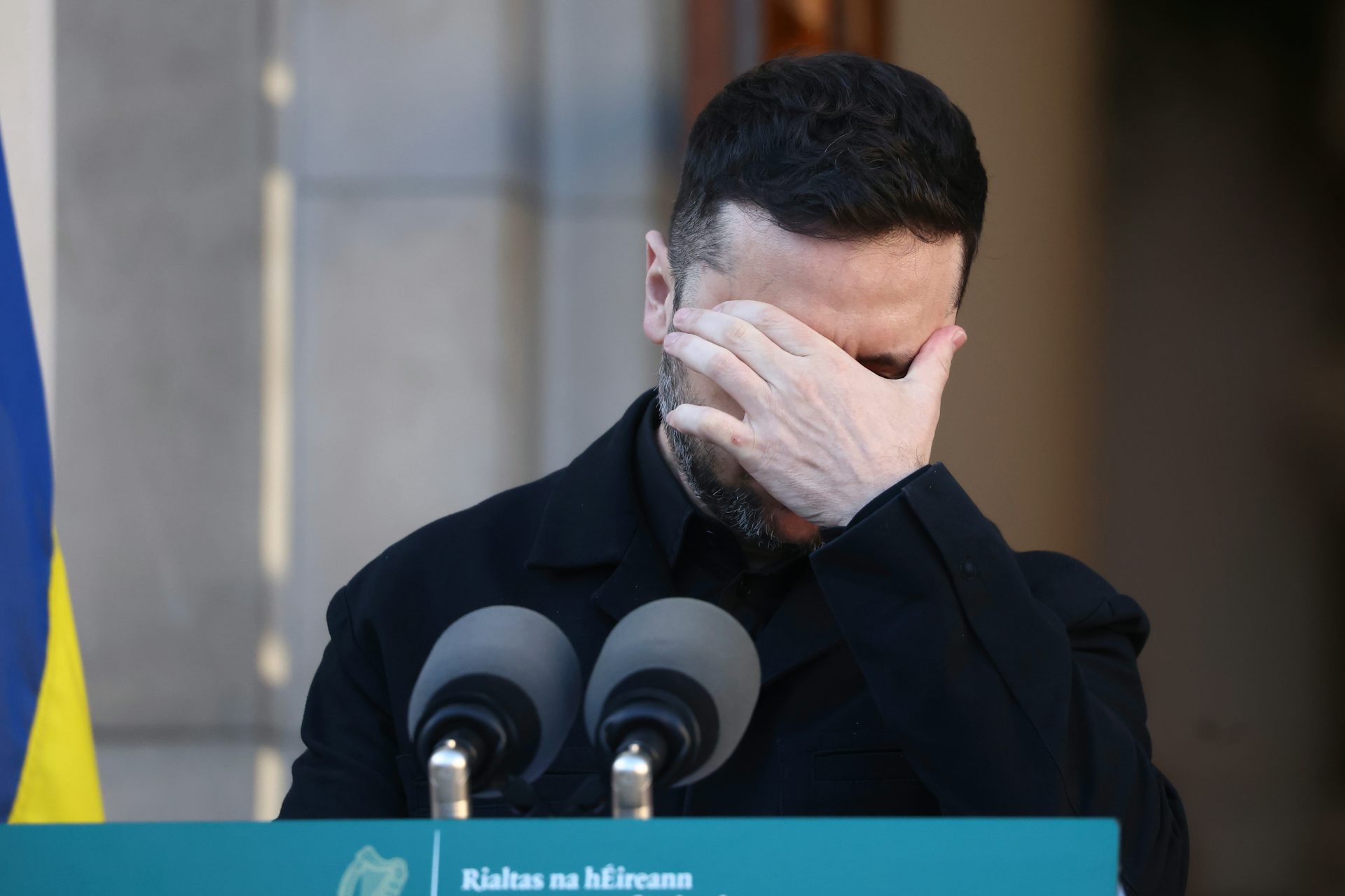 A dark-haired man with his hand over his eyes.