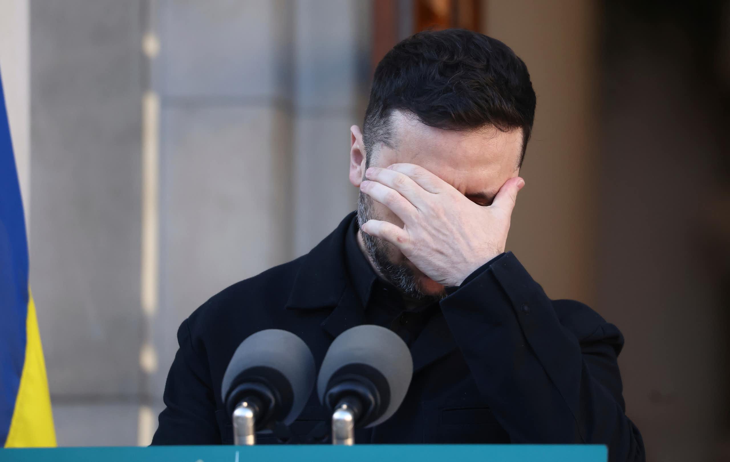 A dark-haired man with his hand over his eyes.