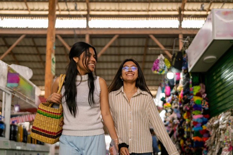 Dos mujeres sonrientes caminan por un mercado.