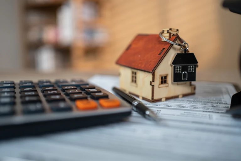 a small housoe with a house key chain on it sit on a table next to a pen and calculator