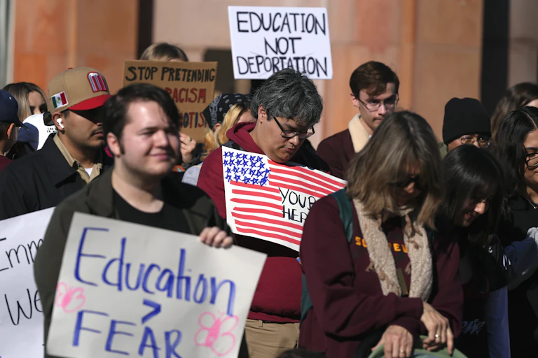 A group of young people stand together and hold signs that say 'Education is greater than fear.'