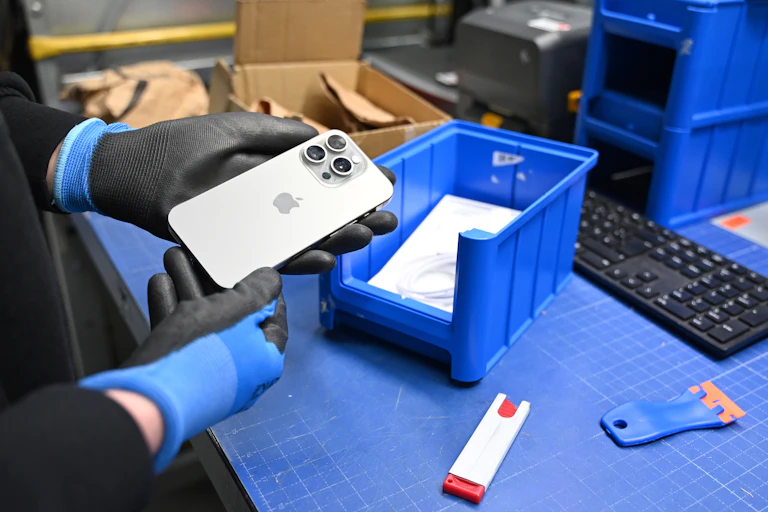 A person wearing plastic gloves holds an iPhone over a plastic blue bin.