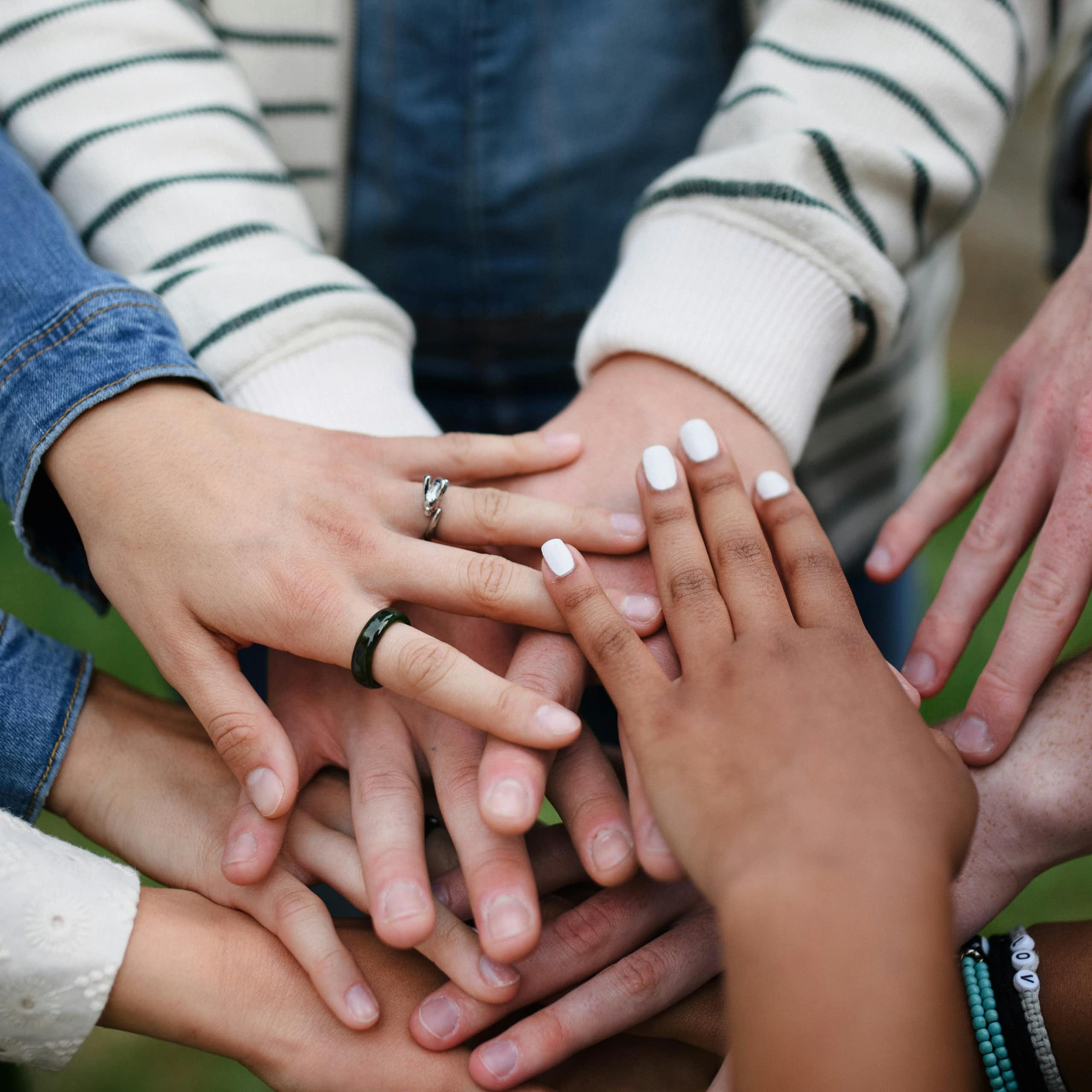 A group of people putting their hands together while standing in a circle