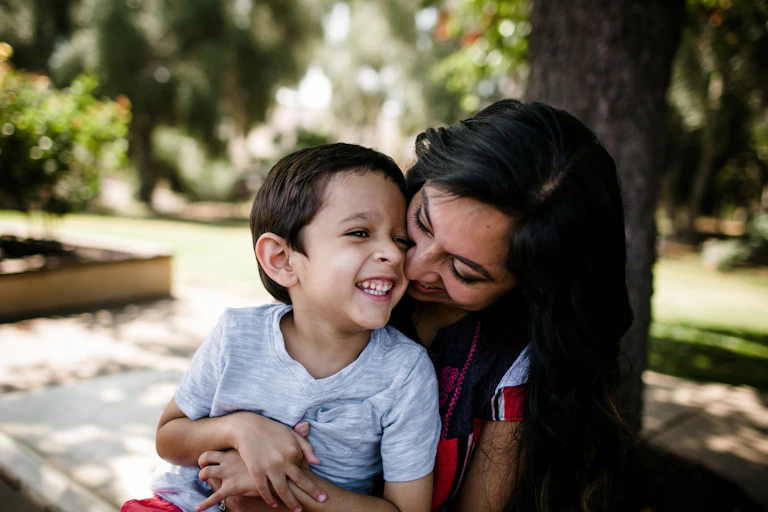 Autistic boy and mother cuddling, laughing, outside in park or garden