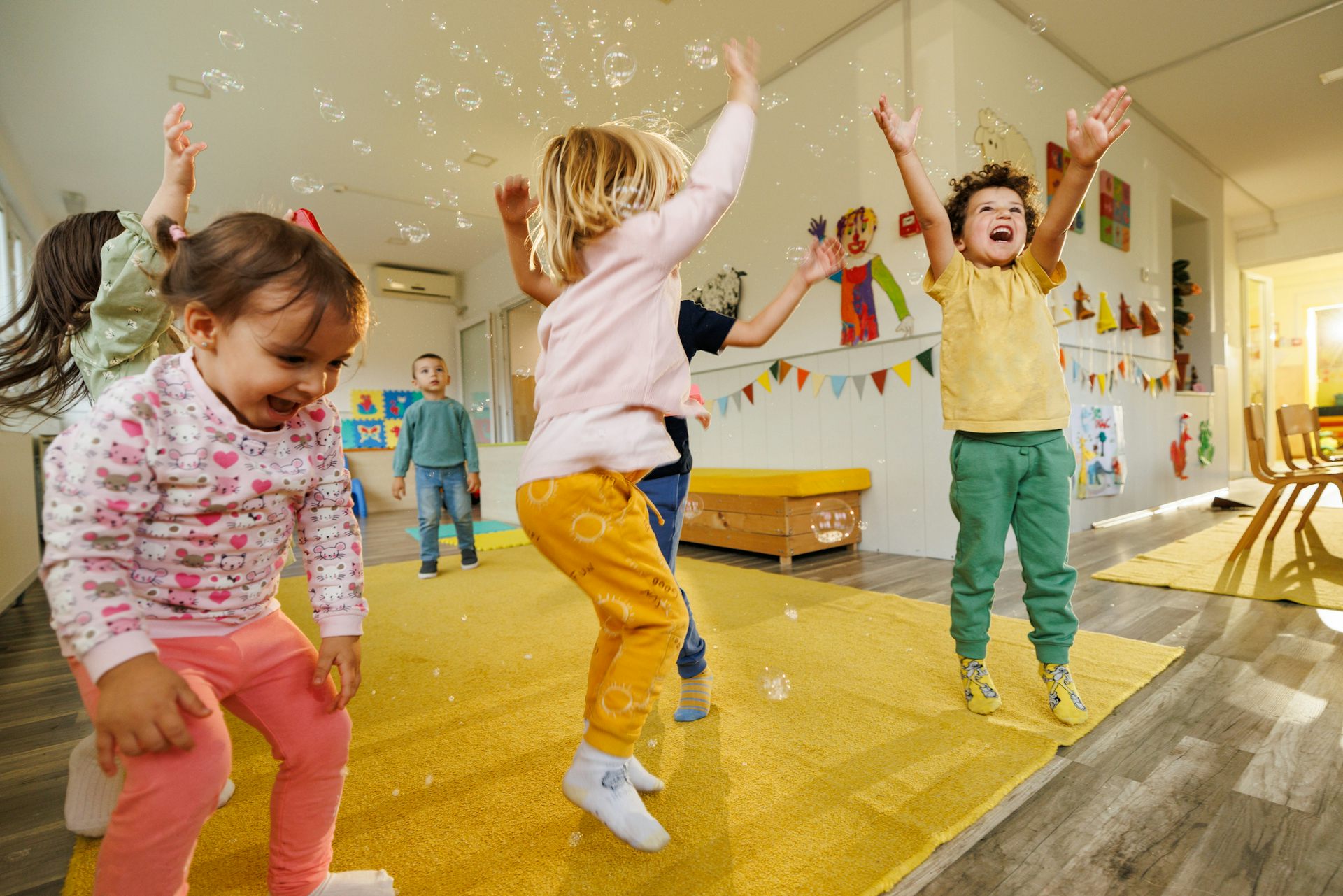 Children jump on a yellow mat in a classroom.
