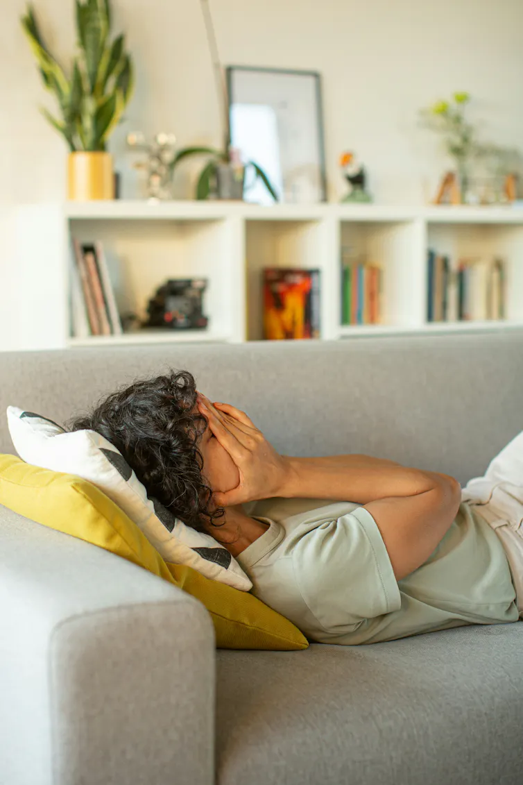 Une femme allongée sur un canapé, les mains sur le visage