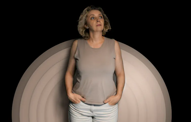 Une femme aux cheveux grisonnants debout devant un cercle beige sur fond noir