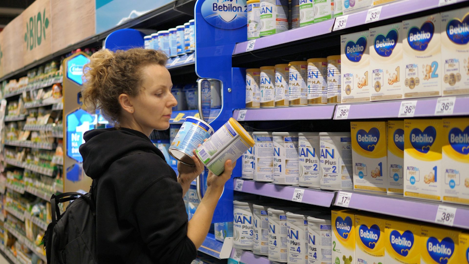A woman looking at various containers of infant formula in a supermarket.