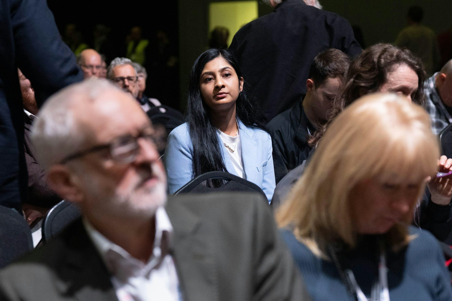 Zarah Sultana sitting several rows behind Jeremy Corbyn in an audience. 