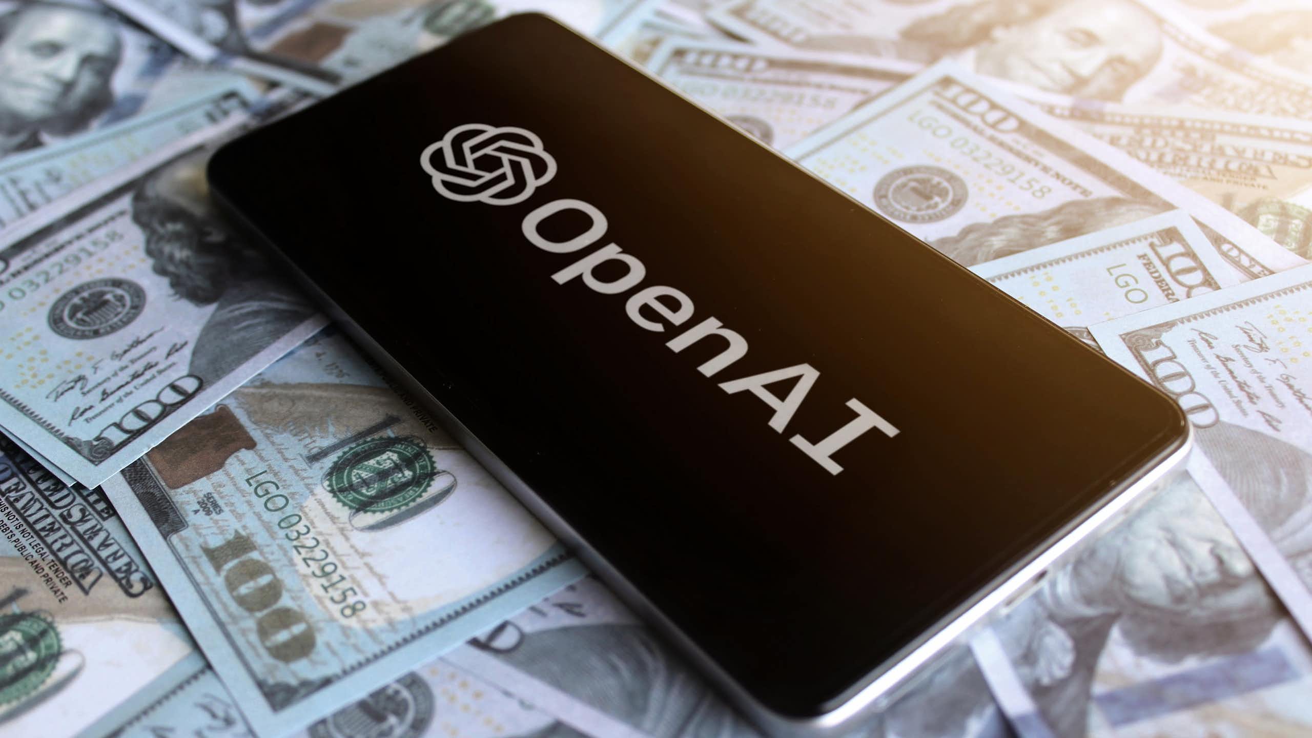 Phone showing OpenAI logo on top of US$100 bills.