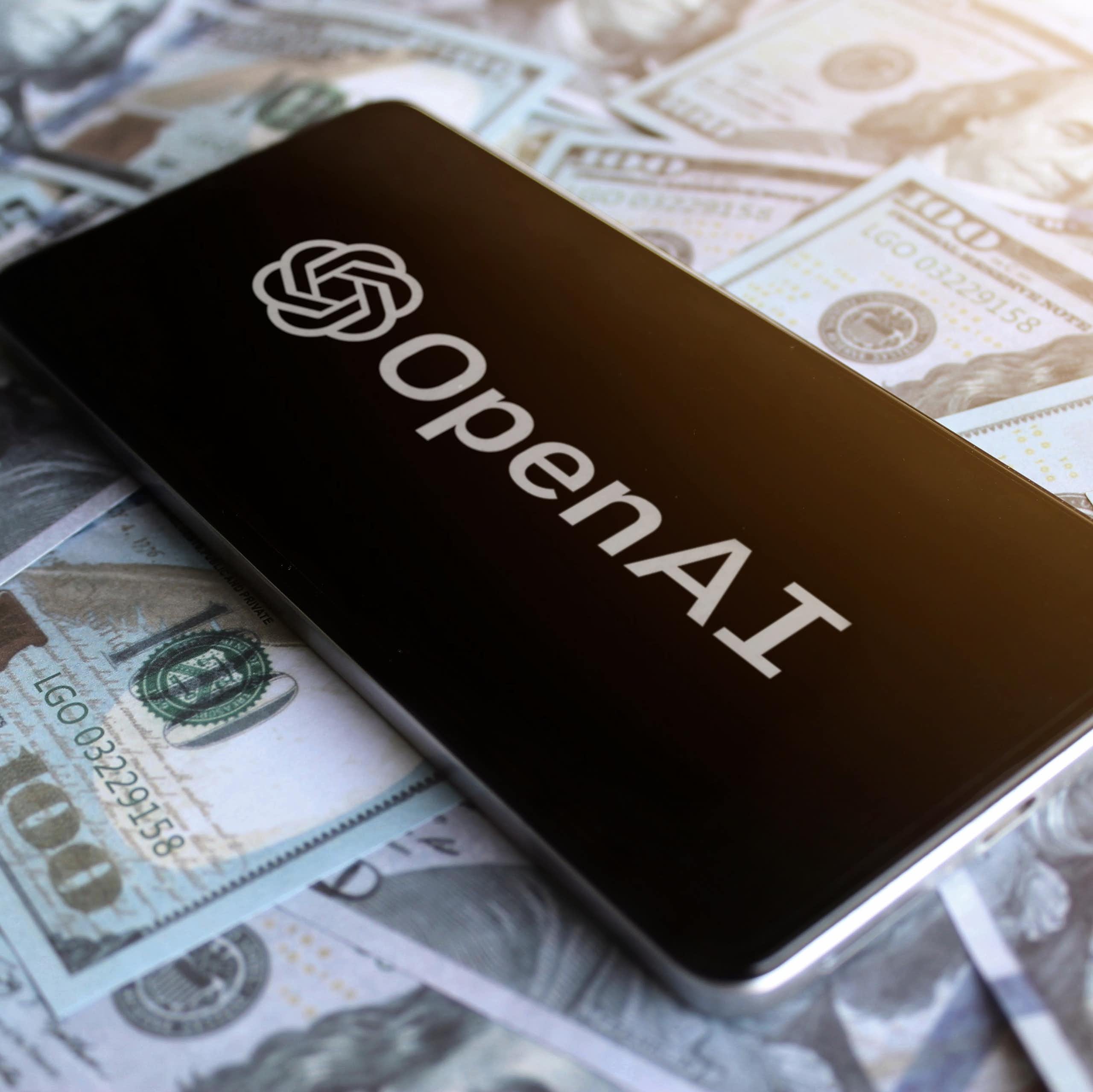 Phone showing OpenAI logo on top of US$100 bills.