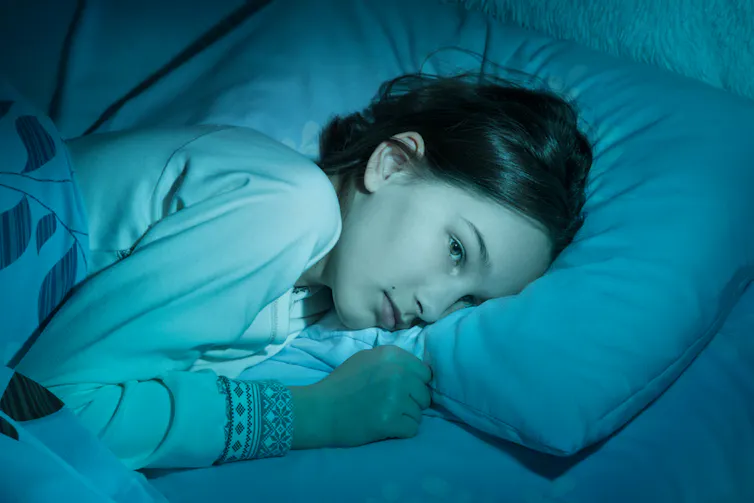 A young girl lying awake in bed.