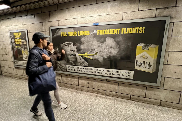 people walk past fossil fuel ad in tube station