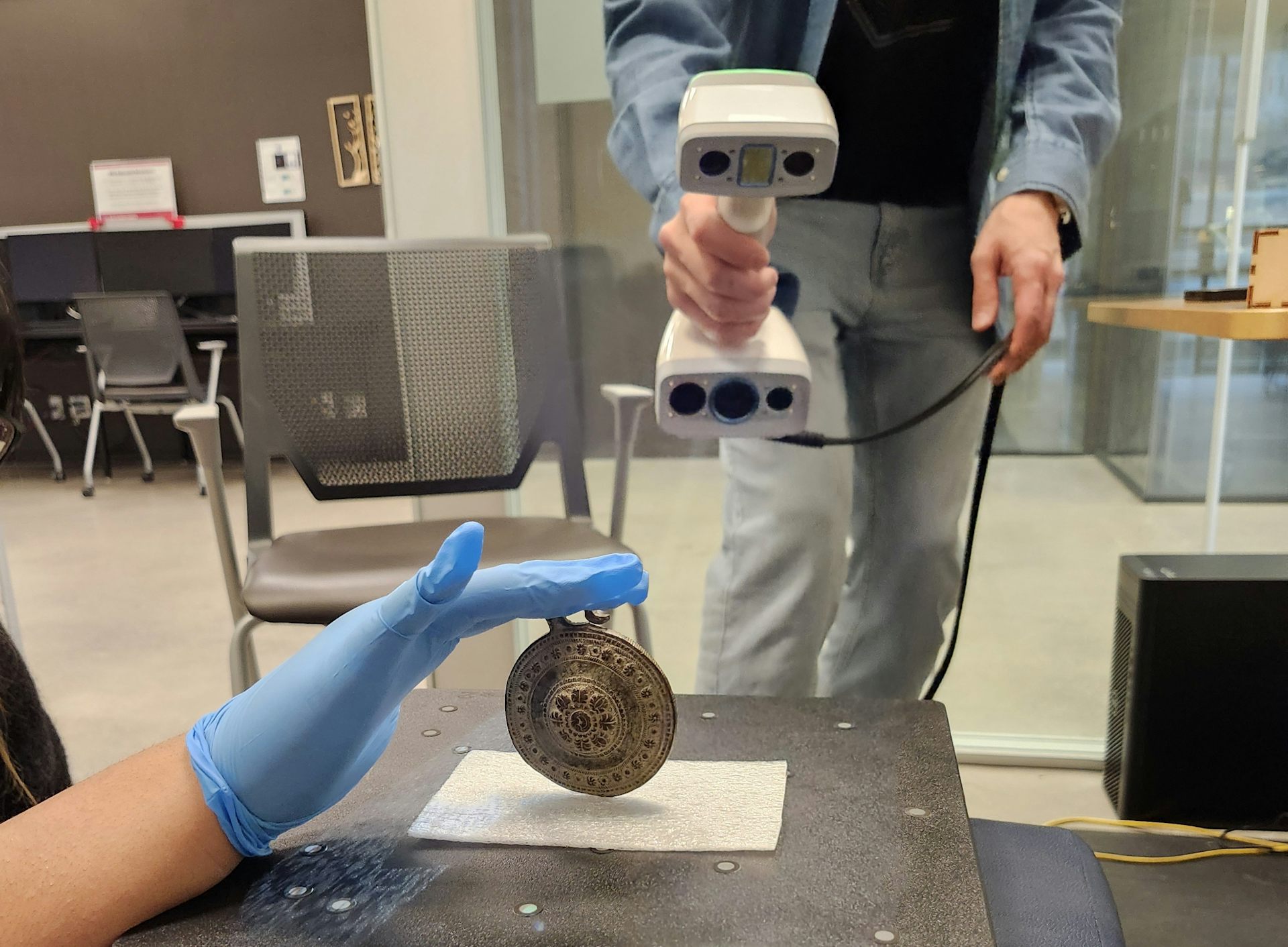 Las manos sostienen un escáner y las otras manos sostienen un relicario redondo.