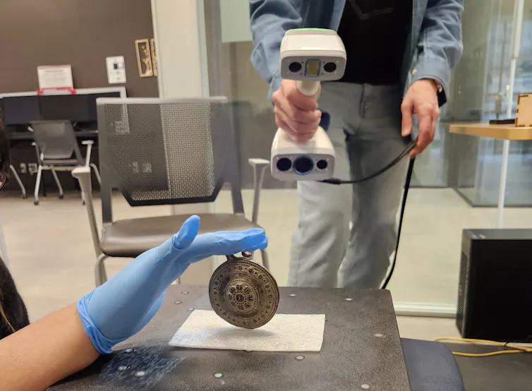 Hands holding a scanner and other hands holding a round medallion.