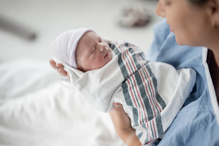 Newborn baby wrapped in hospital blanket in the hands of a caregiver