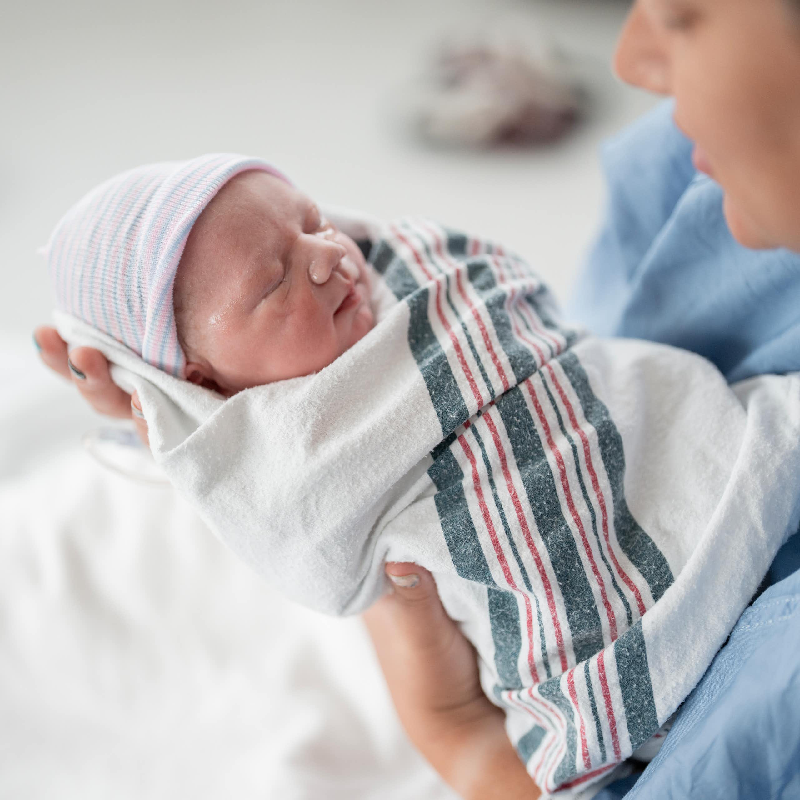 Newborn baby wrapped in hospital blanket in the hands of a caregiver