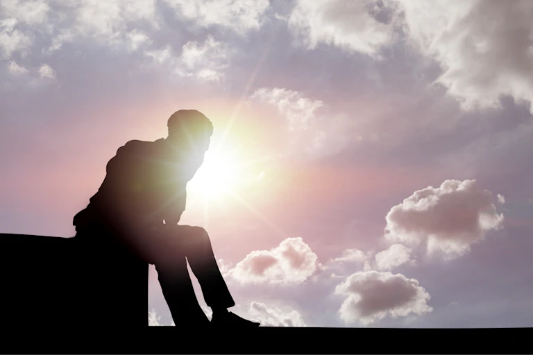 silhouette of a man sitting on a structure against a bright sunny sky